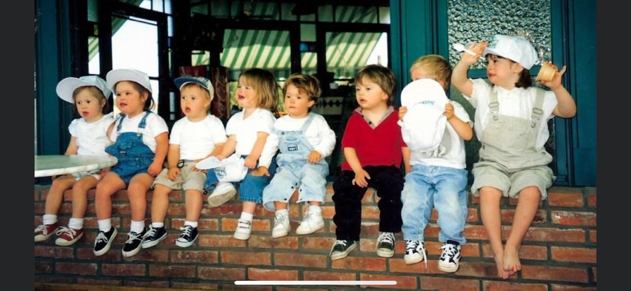 8 niños con síndrome de Down sentados en una pared de ladrillos