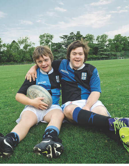 Muchachos con síndrome de down sentados en la cancha de rugby con la pelota en la mano